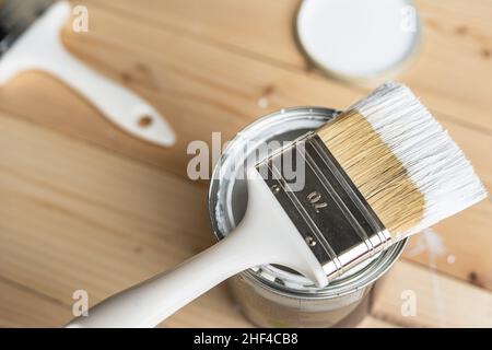 Draufsicht auf weißem Pinsel auf der geöffneten Dose Auf dem Holztisch oder Bodenbemalung und Renovierung Reparatur Konzept Stockfoto