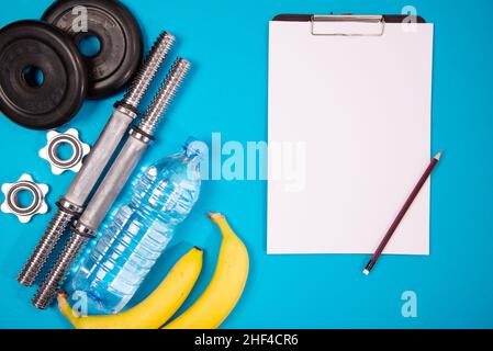 Fitness oder Bodybuilding. Sportausrüstung auf blauem Hintergrund, Banane, Flasche Wasser, Langhantel, Kurzhantel, Draufsicht mit Platz zum Kopieren. Stockfoto