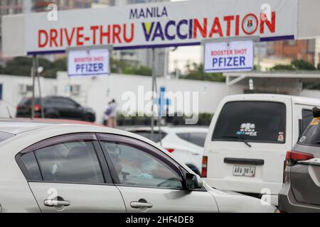 Manila, Philippinen. 14th Januar 2022. Eine Frau, die eine Schutzmaske trägt, blickt aus dem Fenster eines Autos, während sich Autofahrer anstellen, um am 14. Januar 2022 an einer Drive-Thru-Impfstelle in Manila, Philippinen, COVID-19-Impfstoffe zu erhalten. Coronavirus-Infektionen nehmen unter der strikten Durchsetzung der Gesundheitsprotokolle durch die Regierung weiter zu. Heute wurden mehr als 37.000 Fälle registriert, der höchste seit Beginn der Pandemie. (Bild: © Basilio Sepe/ZUMA Press Wire) Stockfoto