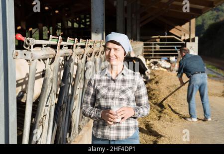 Lächelnde reife Bäuerin mit Kuhmilch im Glas Stockfoto
