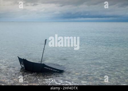 Ein schwarzer Regenschirm wurde an einem walisischen Strand gewaschen Stockfoto