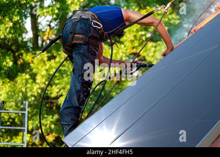 Arbeiter waschen Photovoltaikpaneele auf dem Dach mit Druckwasser Stockfoto