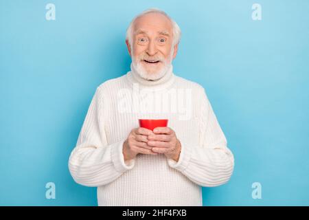 Porträt von attraktiven lustigen fröhlich froh grauhaarigen Mann trinken heißen Cappuccino isoliert über hellen blauen Hintergrund Stockfoto