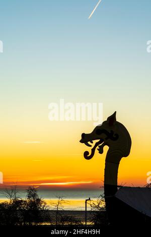 Der Morgenhimmel bei Tagesanbruch über dem Ärmelkanal mit der Silhouette der Galionsfigur, einem Drachenkopf des Wikingerschiffs „Hugin“ in Pegwell Bay, Ramsgate, an der englischen Küste von Kent. Stockfoto