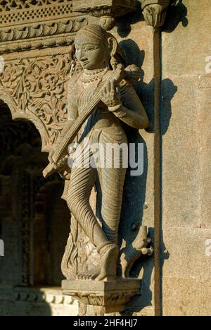 Frau spielt ein in Stein gemeißeltes Veena-Musikinstrument an der Wand des Maheshwar-Tempels Stockfoto