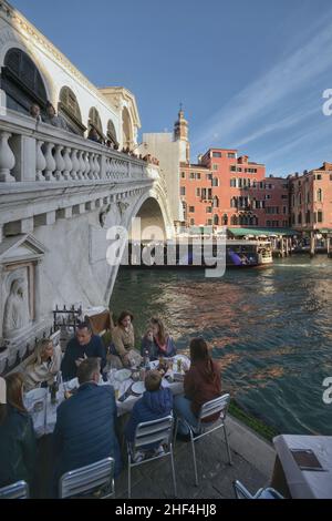 rialtobrücke mit Touristen, die spazieren gehen und anderen, die in einem Restaurant am Kanalufer zu Mittag essen Stockfoto