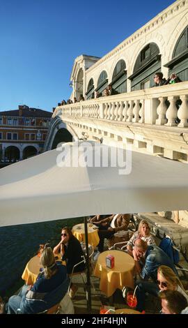 rialtobrücke mit Touristen, die spazieren gehen und anderen, die sich in einer Bar am Kanalufer entspannen Stockfoto