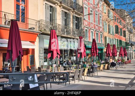Place Carnot, Carcassonne Aude France 01.13.22 strahlender Wintertag. Cafés mit Sitzgelegenheiten im Freien. Reihe roter Parasols. Elegante, farbenfrohe Gebäude Stockfoto
