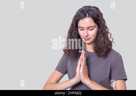 Das Porträt eines hoffnungsvollen Mädchens mit lockigen Haaren hält ihre Hände in einer Gebetsgeste zusammen. Huldigt, betet den Buddha an, grüßt, drückt ein apolo aus Stockfoto