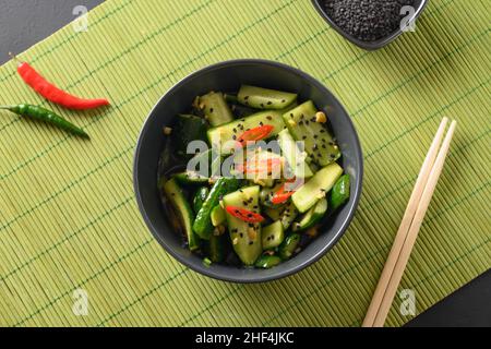 Asiatischer würziger, gebrochener Gurkensalat mit Koriander, Ingwer, Pfeffer-Chili, schwarzem Essig in schwarzer Schüssel auf grüner Matte. Traditionelles kaltes Chinesisch und Vietnam Stockfoto