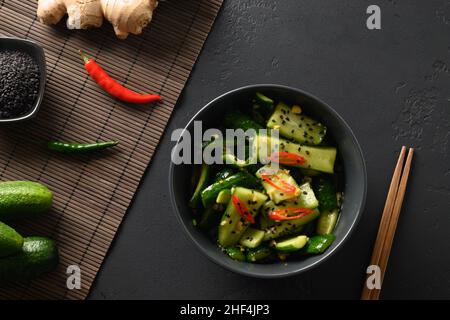 Asiatischer würziger Salat mit gebrochener Gurke mit Korianderblättern, Ingwer, Pfeffer, Chili und Essig auf schwarzem Hintergrund. Würzige Gurken. Beliebte chinesische Vorspeise Stockfoto