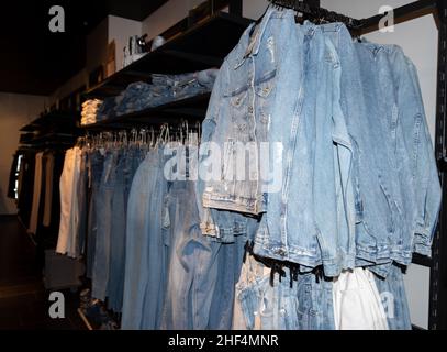 Viele Denim-Jacken hängen im Laden an einem Kleiderbügel. Verschiedene blaue Denim-Jacken auf einem Kleiderbügel in einem Bekleidungsgeschäft. Jeans-Shop. Geschäftskonzept Stockfoto