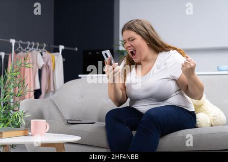 Schwül Plus Größe Frau erhielt positive Nachrichten am Telefon und ist sehr glücklich. Body positive Female Model hält ein Smartphone in der Hand und schreit fröhlich ins Telefon. Nahaufnahme. Hochwertige Fotos Stockfoto