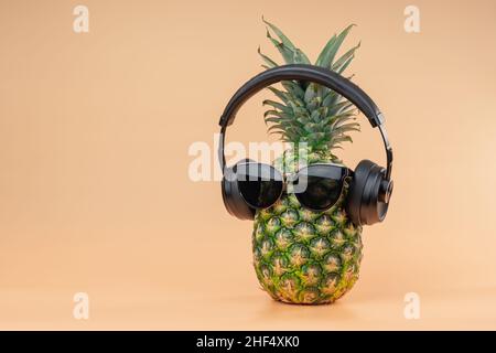 Kreative Idee eines Ananas Bild einer Person Kopfhörer und Brille als entspannender Tourist im Urlaub. Auf gelbem Hintergrund. Stockfoto