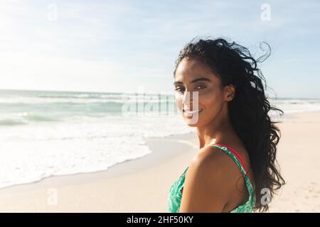 Porträt einer lächelnden, schönen jungen Birazialfrau, die über die Schulter auf den Strand blickt und einen sonnigen Tag genießt Stockfoto