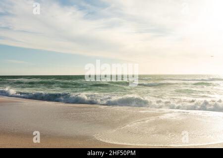 Am Strand plätschern Meereswellen gegen den Himmel und Wolken am sonnigen Tag Stockfoto