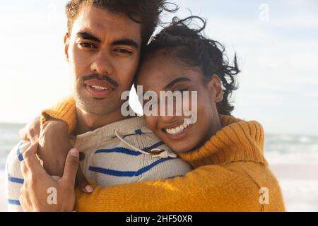 Portrait eines lächelnden Biracial Paares, das sich umarmt, während er einen sonnigen Tag am Strand genießt Stockfoto