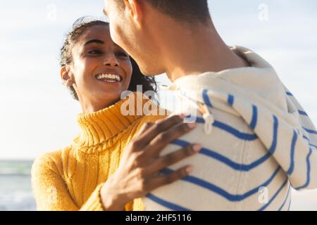 Glückliche biracial junge Frau suchen Freund, während umarmt ihn am Strand an sonnigen Tag Stockfoto