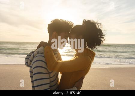 Seitenansicht eines liebenden Biracial Paares, das während des Sonnenuntergangs von Angesicht zu Angesicht am Strand steht Stockfoto