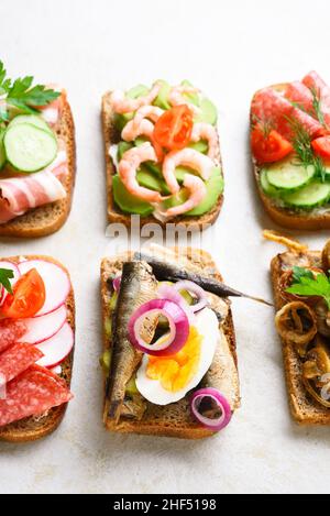 Set aus verschiedenen Sandwiches mit Fleisch, Gemüse, Meeresfrüchten auf hellem Stein Hintergrund. Nahaufnahme Stockfoto