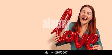 Porträt der romantischen 30s Frau mit Spaß roten Folie Liebe Wort Ballons über beige mit Kopie Raum Hintergrund. Emotionen Stockfoto