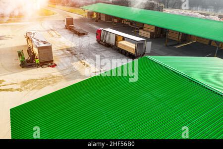 LKW im Fertigwarenlager werden von oben mit Brettern beladen. Stockfoto
