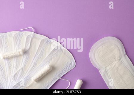 Weiblicher Menstruationsschutz Pack mit Tampons, Baumwollpads, Save Slip und weißer Blume auf fliedernem Hintergrund. Draufsicht. Stockfoto