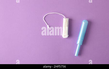 Weicher, schützender und saugfähiger Tampon aus Baumwolle für die Damenpflege auf fliedernem Hintergrund. Draufsicht. Horizontale Zusammensetzung. Stockfoto