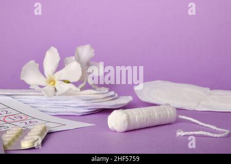 Gruppe von Produkten für den Schutz und die Menstruationshygiene mit Tampons, Wattepads, Save slip und weiße Blume auf lila Hintergrund. Vorderansicht. Stockfoto