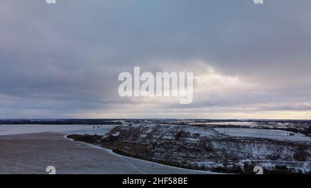 Fliegen über ein schneebedecktes Feld. Die Müllkippe der Stadt ist sichtbar, mit Schnee bedeckt. Mülldeponie mit Mottballenabfällen. Luftaufnahmen. Stockfoto