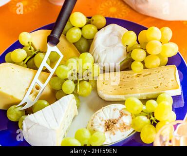 Käseplatte mit Trauben und Messer auf einem blauen Teller Stockfoto