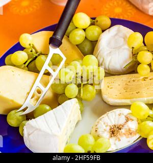 Käseplatte mit Trauben und Messer auf einem blauen Teller Stockfoto