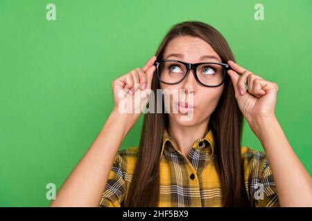 Portrait von gesinnten jungen Mädchen Hände berühren Brillen schauen interessiert leeren Raum auf grünem Hintergrund isoliert Stockfoto