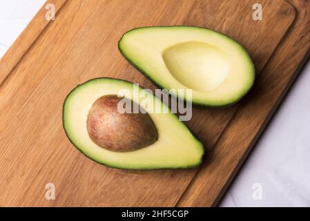 Zwei Avocado-Teile auf Holztisch, halbiert, Samen sichtbar Stockfoto