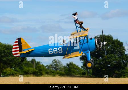 Sarah Niles wingWalking auf einem Boeing Stearman-Flugzeug am Damyns Hall Aerodrome mit Aerobatic Tactics. Mädchen auf dem Flügel, Flügel zu Fuß. Bodennähe Stockfoto