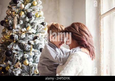 Kleiner Vorschuljunge, der Großmutter hilft, Weihnachtsbaum zu Hause zu schmücken, Großmutter und kleiner Enkel, die zusammen Weihnachtsbaum dekorieren, junge Familie Stockfoto