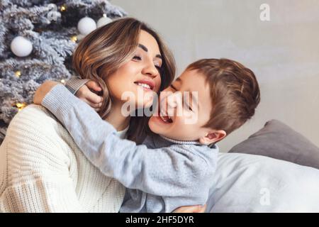 Kleiner Vorschuljunge, der Mutter hilft, Weihnachtsbaum zu Hause zu schmücken, Mutter und kleiner Sohn dekorieren Weihnachtsbaum zusammen, junge Eltern und ch Stockfoto