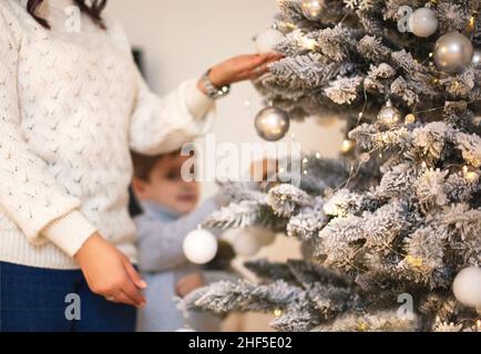 Kleiner Vorschuljunge, der Großmutter hilft, Weihnachtsbaum zu Hause zu schmücken, Großmutter und kleiner Enkel, die zusammen Weihnachtsbaum dekorieren, junge Familie Stockfoto