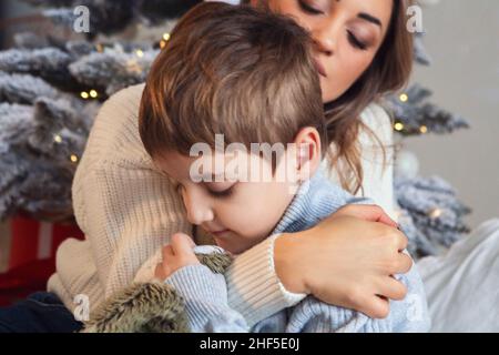 Kleiner Vorschuljunge, der Mutter hilft, Weihnachtsbaum zu Hause zu schmücken, Mutter und kleiner Sohn dekorieren Weihnachtsbaum zusammen, junge Eltern und ch Stockfoto