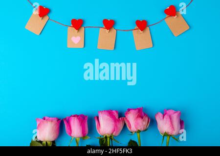 Overhead-Ansicht von frischen rosa Rosen und herzförmige Dekoration auf blauem Hintergrund, Copy Space Stockfoto