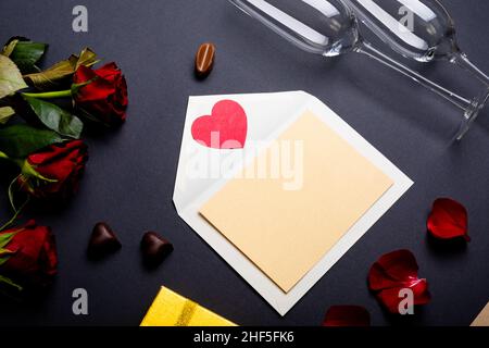 Leerer Brief mit Sektflöten und roten Rosen auf dem Tisch, Platz zum Kopieren Stockfoto