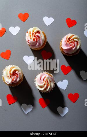 Ansicht von Cupcakes und herzförmiger Dekoration isoliert auf grauem Hintergrund, Kopierraum Stockfoto