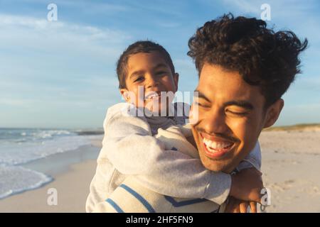 Nahaufnahme eines glücklichen biracial Vater, der Sohn Huckepack Fahrt auf den Sohn am Strand gegen den Himmel Stockfoto