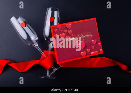Valentinstags-Geschenkkarte mit Sektflöten, eingewickelt mit rotem Band auf schwarzem Tisch mit Platz zum Kopieren Stockfoto