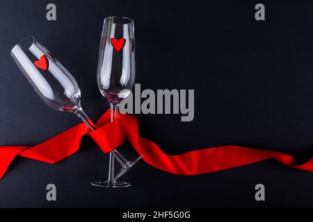 Herzformen in leeren Champagnerflöten, umhüllt mit rotem Band, durch Copy Space auf schwarzem Hintergrund Stockfoto
