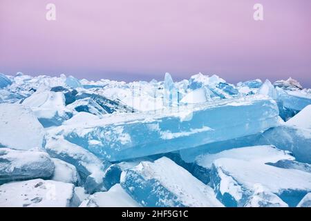 Wunderschöne Landschaft mit großen blauen Peace of Ice-Hummock und Rissen am gefrorenen See mit purpurem Morgenhimmel Stockfoto