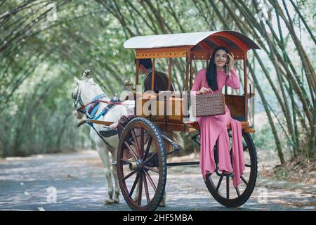 Ho-Chi-Minh-Stadt, Vietnam: Vietnamesische Mädchen tragen weiße AO dai und reiten in einer Pferdekutsche auf einer Landstraße in Vietnam Stockfoto