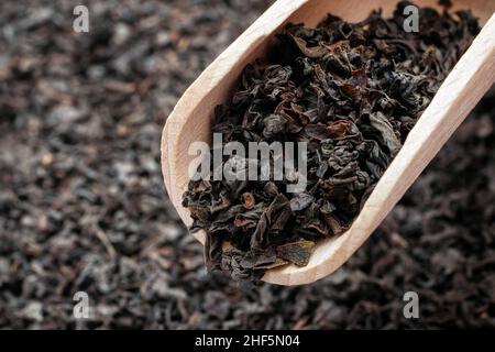 Trocknen Sie Tee mit langen Blättern in einer Holzlöffel. Makro von losem schwarzem Tee. Stockfoto