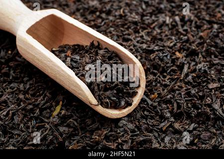 Trocknen Sie Tee mit langen Blättern in einer Holzlöffel. Makro von losem schwarzem Tee. Stockfoto