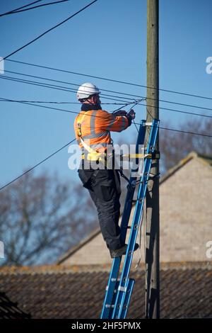 Ein offener Telekommunikationsingenieur bei der Arbeit auf einer Leiter trägt er die richtige PSA für die Arbeit in der Hand und erfüllt gleichzeitig die H&S-Vorschriften. Stockfoto